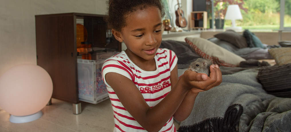 Een meisje houdt haar hamster vast met een Qute kooi op de achtergrond
