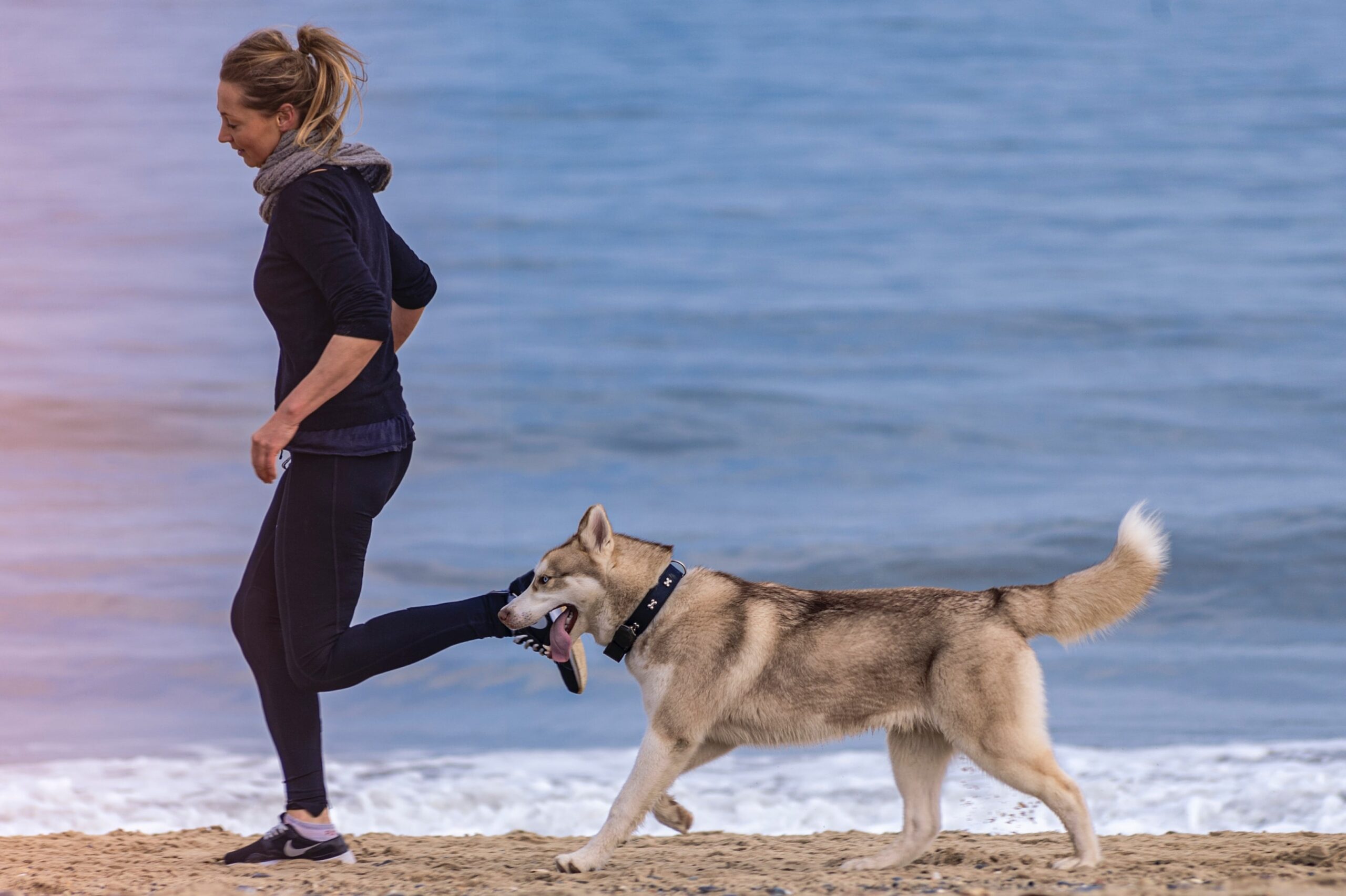 Een vrouw aan het hardlopen op het strand met haar hond