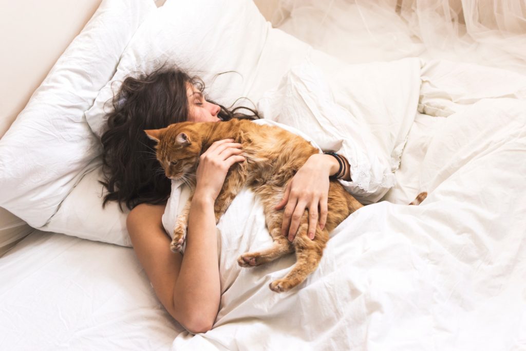 Vrouw slapend in bed terwijl ze knuffelt met een kat
