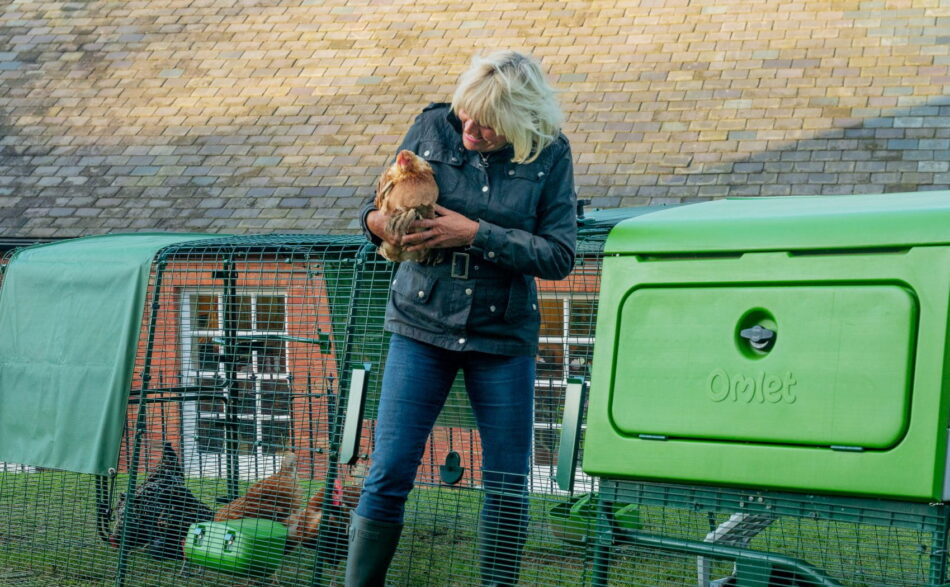 Vrouw met een kip in haar handen die uit de ren van het Eglu Pro kippenhok stapt