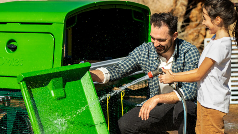 Man en meisje maken het Omlet Eglu Pro-zitrek schoon met een tuinslang
