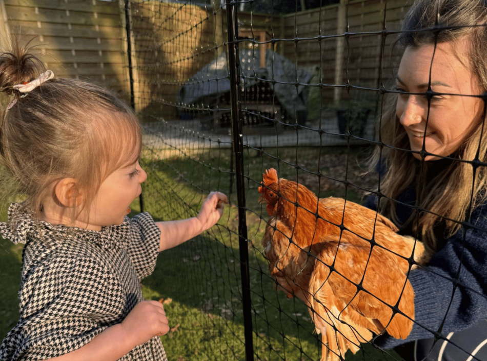 Louise en haar dochter kijken naar een kip door de afrastering van Omlet